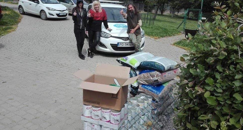 Freskowe zdjęcie z pracownikami Oxynet Jarosław przy zbiórce i transporcie artykułów budowlanych i materiałów remontowych. Na zdjęciu widać samochody, pakiety cementu, worki z materiałami, oraz uśmiechniętych ludzi przy projekcie społecznym i pomocy dla lokalnej społeczności.